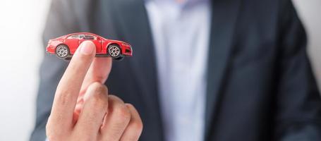 affärsman hand som håller röd bil leksak. bilförsäkring, garanti, uthyrning, finansiellt, nytt och reparationskoncept foto