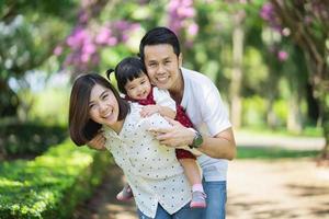 vackra asiatiska familjeporträtt leende och glad. föräldrar kastar dotter i trädgården. lycklig familj koncept. foto