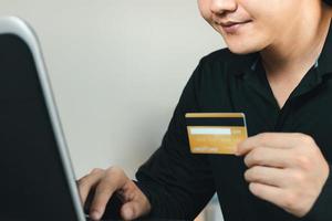 online shopping koncept. ung man skriver ett onlinebetalningsnummer från sitt kreditkort till sin bärbara dator. foto