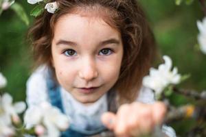 en söt liten flicka på 5 år i en blommande vit äppelodling på våren. vår, fruktträdgård, blomning, allergi, vårdoft, ömhet, omsorg om naturen. porträtt foto