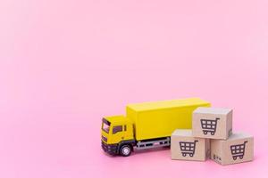 logistik och leveransservice - lastbil och papperskartonger eller paket med en kundvagnslogotyp på rosa bakgrund. shoppingtjänst på webben och erbjuder hemleverans. foto