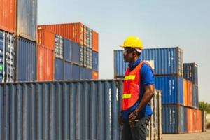 arbetare man i hjälm och skyddsväst står vid containrar last, förman kontroll lastning containrar låda från last foto
