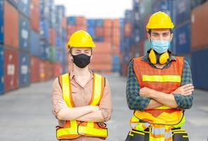 framgång lagarbete koncept, affärsmän ingenjör och arbetar team bär skyddande ansiktsmask mot coronavirus med armarna i kors som tecken på framgång suddig bakgrund i containerlådan foto