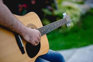 bild av en gitarrist, en ung man som spelar gitarr medan han sitter i en naturlig trädgård, musikkoncept foto