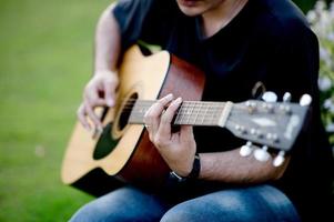 bild av en gitarrist, en ung man som spelar gitarr medan han sitter i en naturlig trädgård, musikkoncept foto