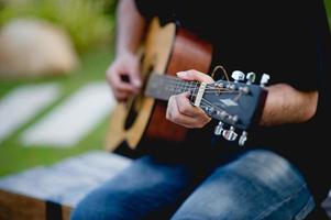 bild av en gitarrist, en ung man som spelar gitarr medan han sitter i en naturlig trädgård, musikkoncept foto