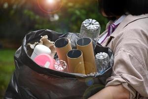 husägaren bär på en svart plastpåse som är full med sopor, plastflaskor, kartonger, mjölkflaskor och använt papper för att separera och hantera sopor hemma. mjukt och selektivt fokus på sopor. foto