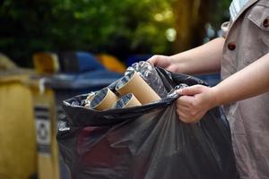 husägaren bär på en svart plastpåse som är full med sopor, plastflaskor, kartonger, mjölkflaskor och använt papper för att separera och hantera sopor hemma. mjukt och selektivt fokus på sopor. foto