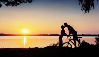 par på en cykel i solnedgången vid sjön foto