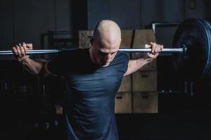 atletisk muskulös man som håller skivstång på dina axlar i gymmet. dramatisk färggradering. foto