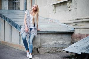 snygg blond kvinna bär på jeans och flicka ärmlös med vit skjorta mot gatan. mode urban modell porträtt. foto