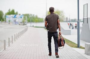 bakifrån porträtt av promenader snygg afrikansk amerikansk man bär på solglasögon och mössa med handväska utomhus. street fashion svart man. foto