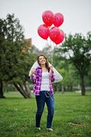 porträtt av brunett tjej på rutig skjorta, jeans och slöja med många röda ballonger på möhippo. foto