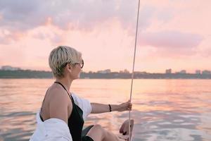 vacker blond glad kvinna njuter av solnedgången på yachten i havet. resor, äventyr, avkoppling koncept foto