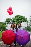 grupp på tre tjejer som har kul på möhippo, med paraply under regn och ballonger. foto