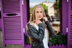 snygg blond kvinna bär på jeans och jacka poserade på gatan mot lila fönster. mode urban modell porträtt. foto