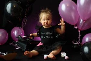 första året flickans födelsedagsfest dag. ballonger och semester inomhus. barnets födelsedag. liten söt flicka i sin första svarta klänning foto