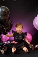 första året flickans födelsedagsfest dag. ballonger och semester inomhus. barnets födelsedag. liten söt flicka i sin första svarta klänning foto
