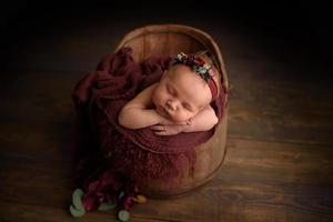 söt nyfödd flicka sover i ett badkar på en trä bakgrund. foto