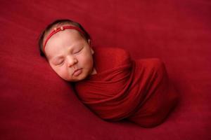 nyfödd flicka sover på en röd trasa i ett rött omslag foto