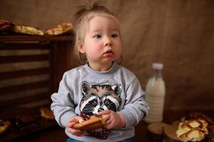 liten flicka i köket äter söta bakverk. foto