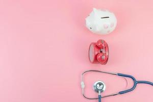ovanifrån med kopia av piggibank, röd klocka och stetoskop på den rosa pastellbakgrunden, besparingar, tid och hälsokoncept foto