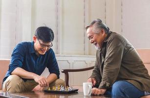 senior asiatisk far och medelålders son spelar schackspel i vardagsrummet, asiatiska familjekoncept för lycka foto