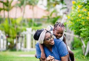 afrikansk amerikansk mamma leker med flickan på ryggen, glad mor och dotter skrattar tillsammans utomhus foto