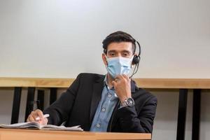 ung telefonist med headset-skydd ansiktsmask mot coronavirus, kundtjänstverkställande team som arbetar på kontoret foto