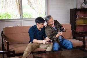 senior asiatisk far och medelålders son spelar videospel tillsammans i vardagsrummet, lycka asiatiska familj koncept foto