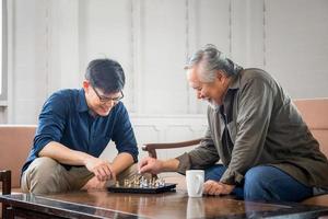 senior asiatisk far och medelålders son spelar schackspel i vardagsrummet, asiatiska familjekoncept för lycka foto