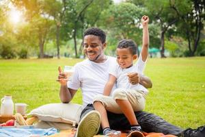 glada afroamerikanska far och son som har en picknick i parken, lycka familjekoncept foto