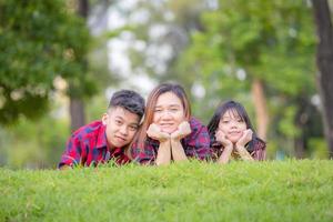 leende mamma och två barn liggande på gräs, glad mamma son och dotter i en park, familjekoncept foto