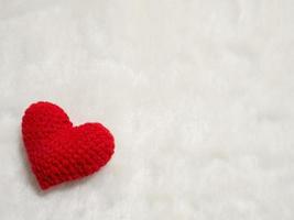 handgjort rött garnhjärta på vit ull. det röda hjärtat i det vänstra hörnet av bilden och bakgrundskopieringsutrymme för text. Alla hjärtans dag, kärlekskoncept och kärleksbakgrund foto