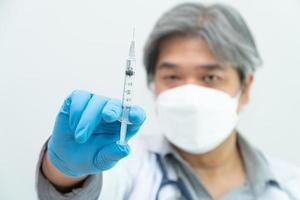en asiatisk manlig läkare bär en medicinsk handske och ansiktsmask som håller i en spruta som tar covid 19 coronavirus-vaccin för att studera och analysera antikroppsprover för patienten. begreppet sjukdomar, sjukvård foto