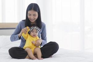 en asiatisk mamma leker med sin bebis i sängen med kärlek och omsorg. foto