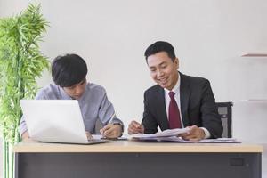 en asiatisk manlig handledare lär nykomlingen till kontoret på sitt skrivbord. foto
