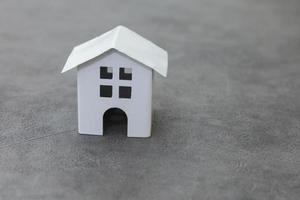 enkelt designa med miniatyr vit leksak modell hus på betong sten grå bakgrund. inteckning fastighetsförsäkring drömhem koncept. kopieringsutrymme. foto