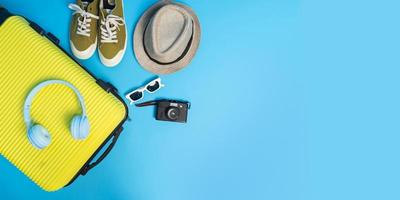 ovanifrån resväska med solglasögon, hatt och kamera på blå bakgrund. resekoncept. foto