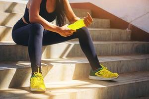 trött löpare kvinna med en flaska elektrolyt dricka friskhet efter träning utomhus träning på stadion trappan. foto