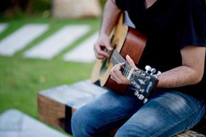 bild av en gitarrist, en ung man som spelar gitarr medan han sitter i en naturlig trädgård, musikkoncept foto