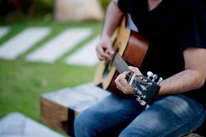 bild av en gitarrist, en ung man som spelar gitarr medan han sitter i en naturlig trädgård, musikkoncept foto