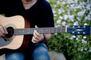 bild av en gitarrist, en ung man som spelar gitarr medan han sitter i en naturlig trädgård, musikkoncept foto