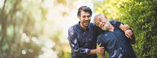 äldre far med vuxen son i familjekoncept bannerbakgrund med kopia utrymme, äldre gammal man person är glad och njuter med hipster son tillsammans genom att gå utomhus i naturen foto