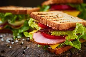 hemlagad smörgås med skinka, sallad, ost och tomat på en träbakgrund foto