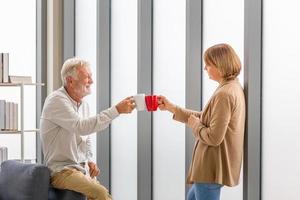 selektivt fokus på kaffekoppen, äldre par i hemmet under en kaffepaus, leende äldre par som rostar en kopp kaffe foto