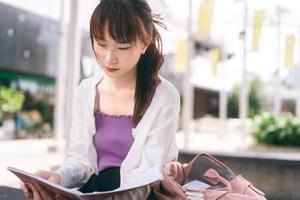 ensamstående ung vuxen asiatisk studentkvinna sitter och studerar med anteckningsboken på campusområdet. foto