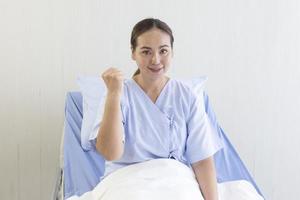 asiatiska kvinnliga patienter ligger på sjukhussängar, räcker upp händer, knytnävar, visar självsäkra symptom foto