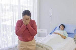 en asiatisk kvinna gråter och sorger bredvid sjukhussängen. foto