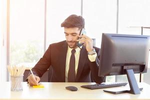 en affärsman i en snyggt klädd kostym sitter i telefonen med ett ljust leende på kontoret foto